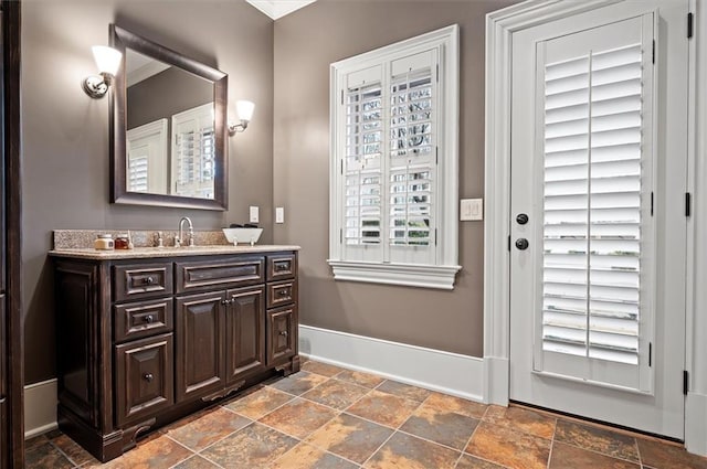 bathroom with stone tile floors, baseboards, and vanity