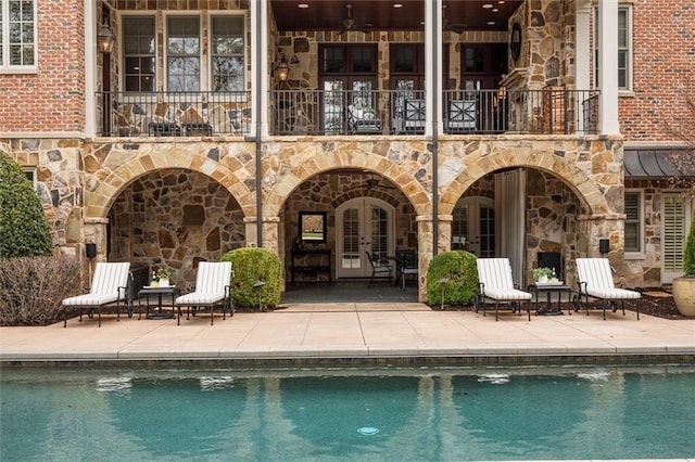 back of property with a balcony, french doors, stone siding, and a patio area