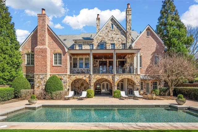 rear view of property featuring stone siding, a balcony, a patio area, an outdoor pool, and french doors