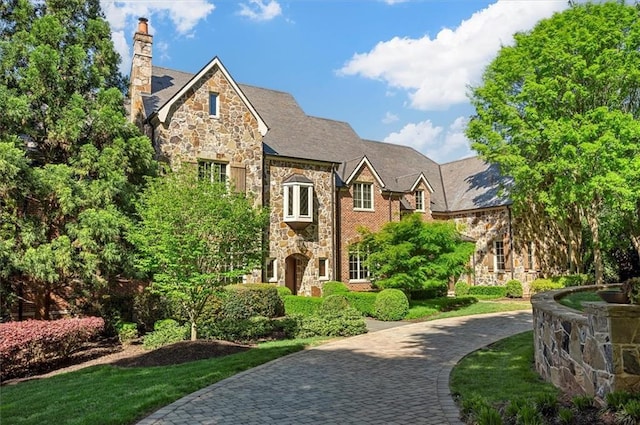view of front facade featuring stone siding, a chimney, and a high end roof