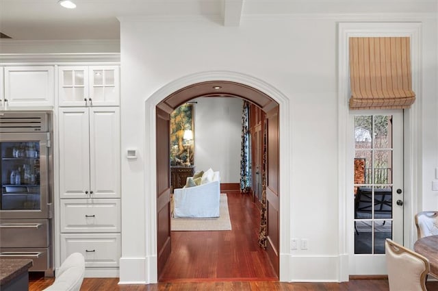 hall featuring arched walkways, wood finished floors, baseboards, ornamental molding, and recessed lighting