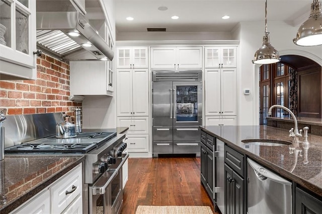 kitchen featuring high end appliances, extractor fan, a sink, white cabinetry, and ornamental molding