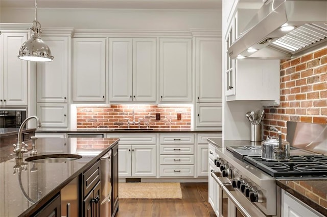 kitchen with wall chimney range hood, a sink, high end stove, white cabinetry, and ornamental molding