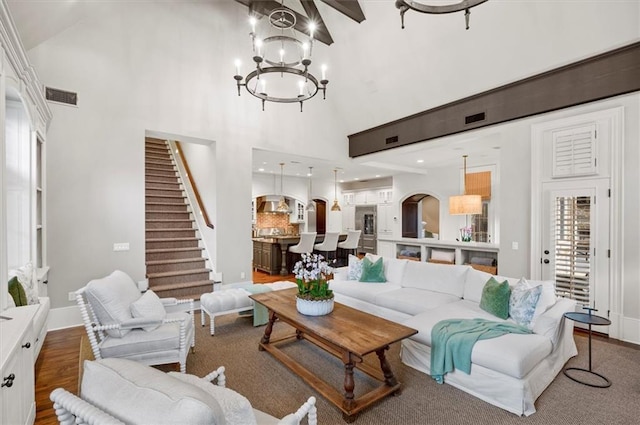 living room featuring high vaulted ceiling, stairs, a chandelier, baseboards, and wood finished floors