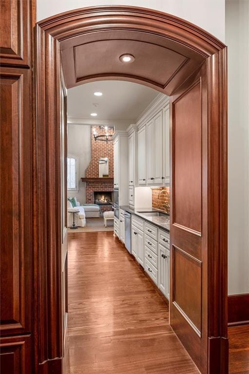 bar featuring dishwasher, a sink, wood finished floors, a brick fireplace, and arched walkways