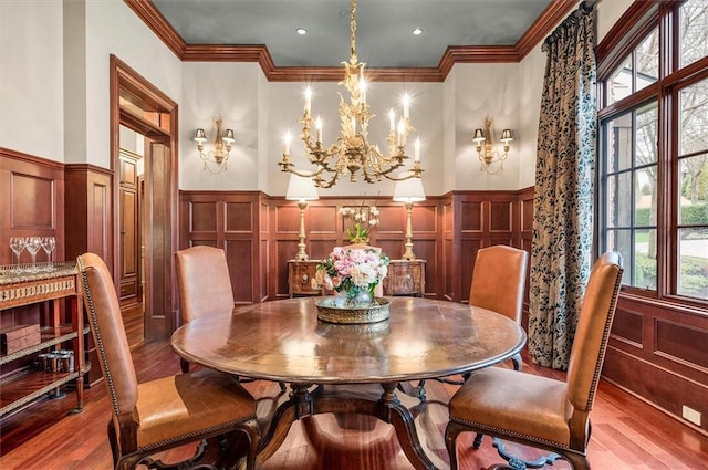 dining room featuring a decorative wall, wainscoting, wood finished floors, a chandelier, and ornamental molding