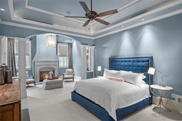 carpeted bedroom featuring ornate columns, arched walkways, a tray ceiling, crown molding, and baseboards