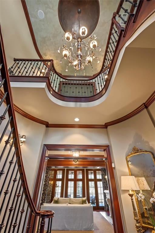 entrance foyer with a towering ceiling, french doors, ornamental molding, and a chandelier