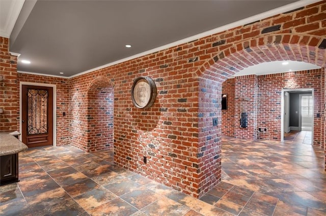 hallway with brick wall, crown molding, recessed lighting, and stone finish flooring
