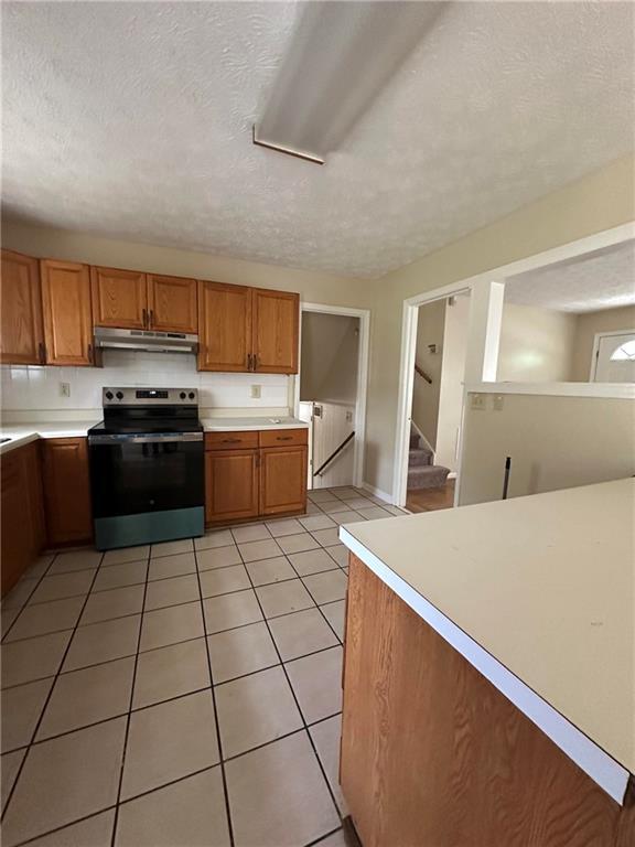 213 Peartree Ln, Riverdale, GA 30274 - kitchen with stainless steel electric range oven, under cabinet range hood, brown cabinets, light countertops, and a textured ceiling