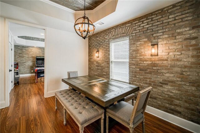 dining space featuring dark wood-type flooring, a chandelier, brick wall, and ornamental molding