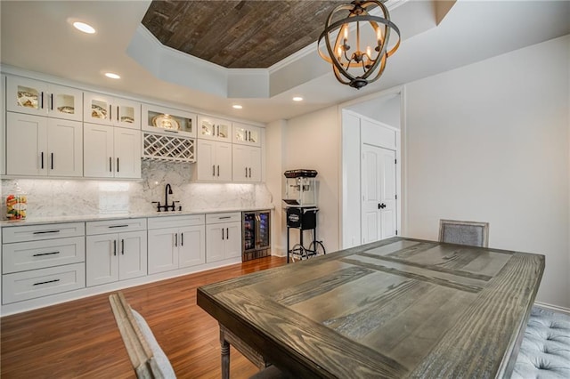 bar featuring crown molding, white cabinetry, a raised ceiling, dark hardwood / wood-style flooring, and hanging light fixtures