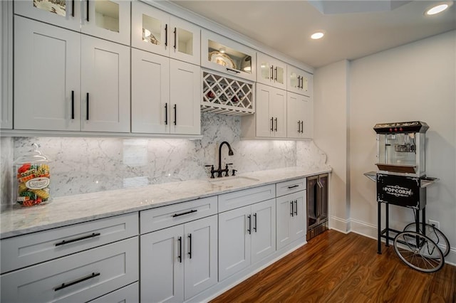 kitchen featuring dark hardwood / wood-style flooring, light stone countertops, decorative backsplash, sink, and white cabinets