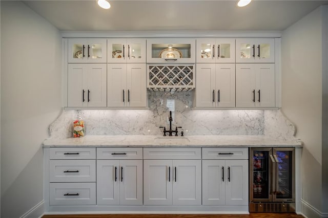 bar featuring light stone counters, white cabinets, sink, backsplash, and wine cooler