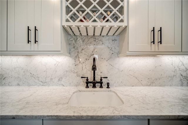 details with white cabinetry, sink, tasteful backsplash, and light stone countertops