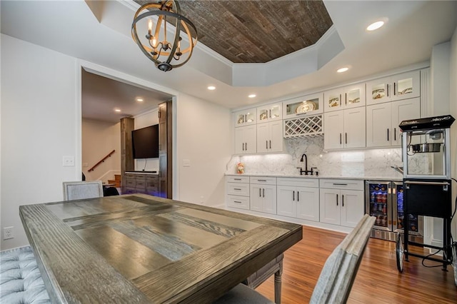 dining space featuring crown molding, wine cooler, a raised ceiling, wet bar, and hardwood / wood-style floors