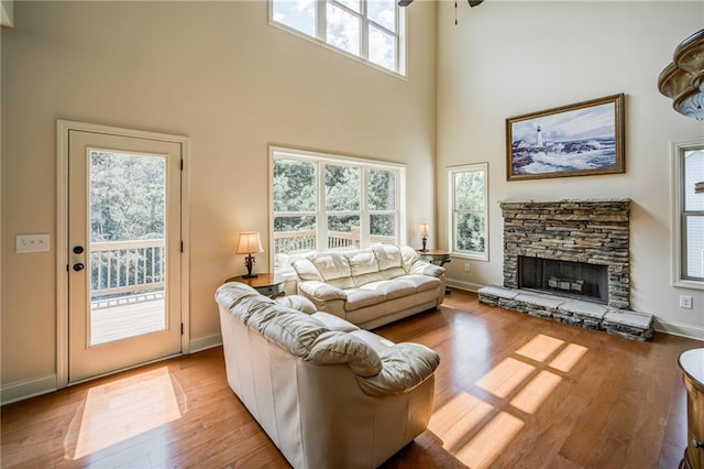 living room with a towering ceiling, a fireplace, light hardwood / wood-style flooring, and ceiling fan