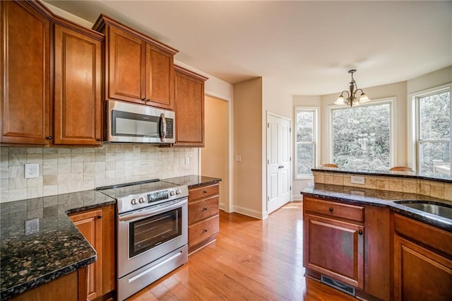 kitchen featuring backsplash, appliances with stainless steel finishes, decorative light fixtures, light hardwood / wood-style floors, and a chandelier