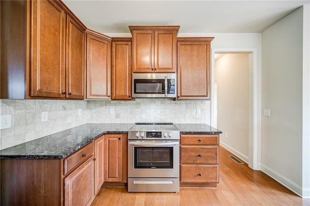 kitchen featuring light hardwood / wood-style flooring, decorative backsplash, dark stone countertops, and stainless steel appliances