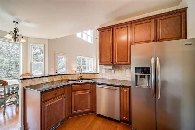 kitchen featuring light hardwood / wood-style floors, sink, appliances with stainless steel finishes, dark stone countertops, and a notable chandelier