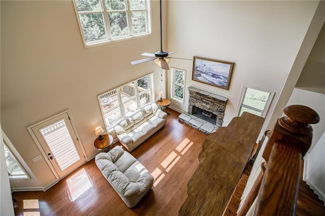 living room with a fireplace, wood-type flooring, ceiling fan, and a towering ceiling