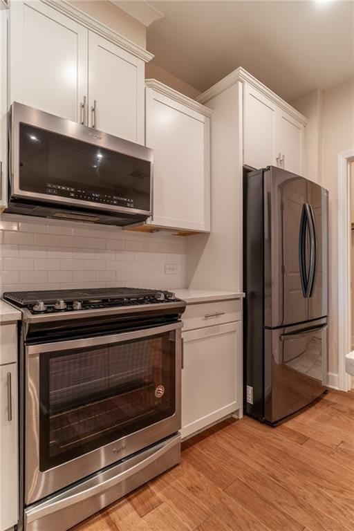 kitchen featuring backsplash, appliances with stainless steel finishes, light hardwood / wood-style floors, and white cabinets