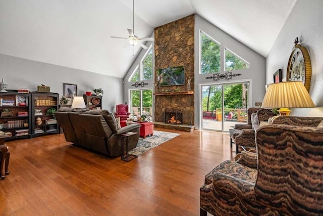 living room with hardwood / wood-style flooring, a stone fireplace, a healthy amount of sunlight, and high vaulted ceiling