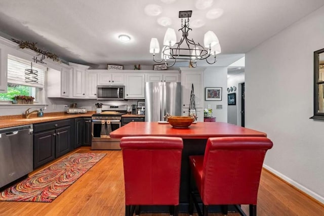 kitchen featuring appliances with stainless steel finishes, decorative light fixtures, light hardwood / wood-style floors, white cabinetry, and an inviting chandelier