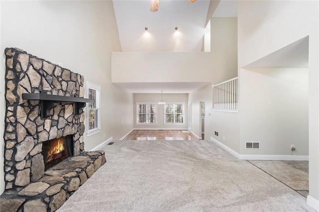 unfurnished living room featuring a towering ceiling, carpet flooring, a stone fireplace, and baseboards