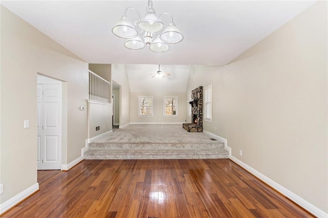 interior space featuring ceiling fan with notable chandelier, vaulted ceiling, baseboards, and wood finished floors