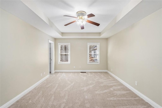 carpeted spare room featuring a raised ceiling, ceiling fan, and baseboards