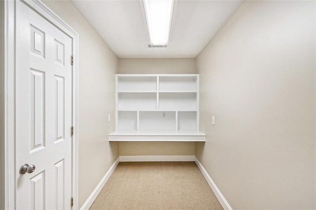 spacious closet with light carpet, visible vents, and built in study area