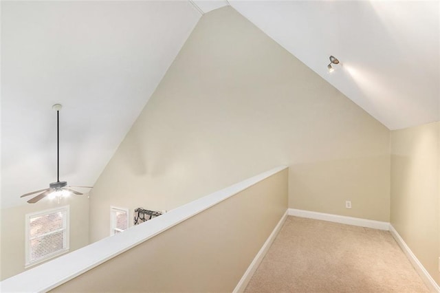 hallway featuring lofted ceiling, light carpet, and baseboards