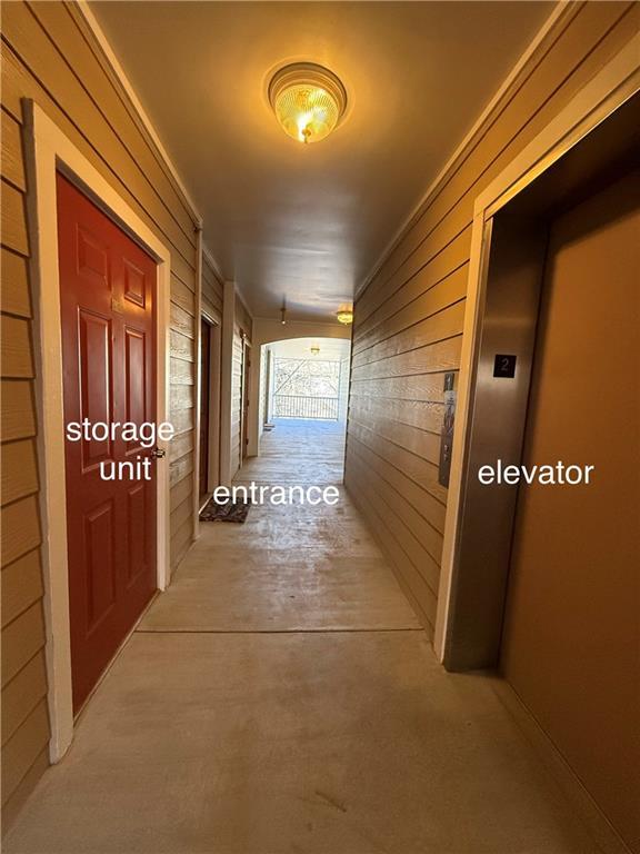 hallway featuring elevator, wood walls, and unfinished concrete floors