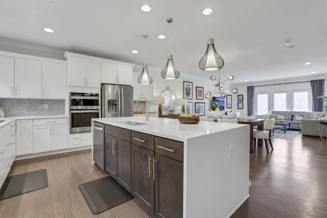 kitchen featuring sink, appliances with stainless steel finishes, hanging light fixtures, white cabinets, and a center island with sink