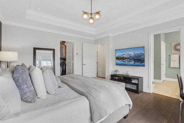 bedroom with ensuite bath, a tray ceiling, dark hardwood / wood-style flooring, a spacious closet, and a chandelier