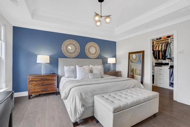 bedroom with hardwood / wood-style floors, a tray ceiling, a notable chandelier, and a closet