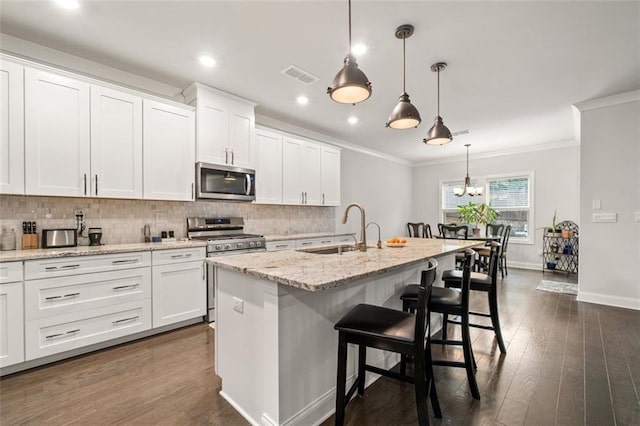 kitchen featuring sink, appliances with stainless steel finishes, an island with sink, white cabinets, and decorative light fixtures