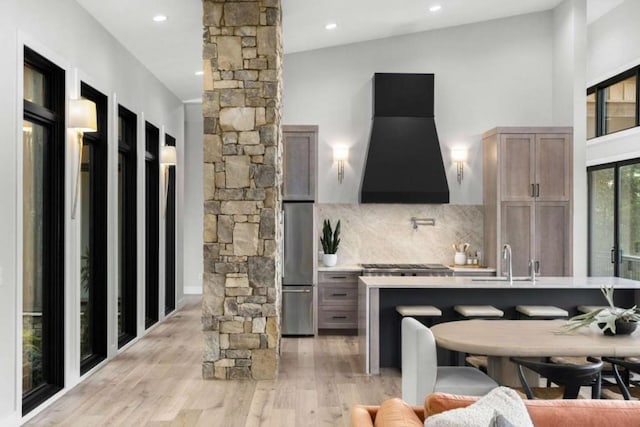 interior space featuring premium range hood, ornate columns, tasteful backsplash, appliances with stainless steel finishes, and light hardwood / wood-style floors