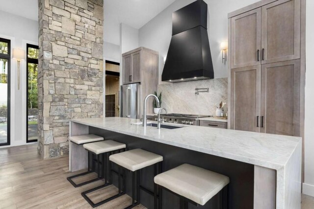 kitchen featuring sink, ventilation hood, light stone countertops, a kitchen bar, and decorative backsplash