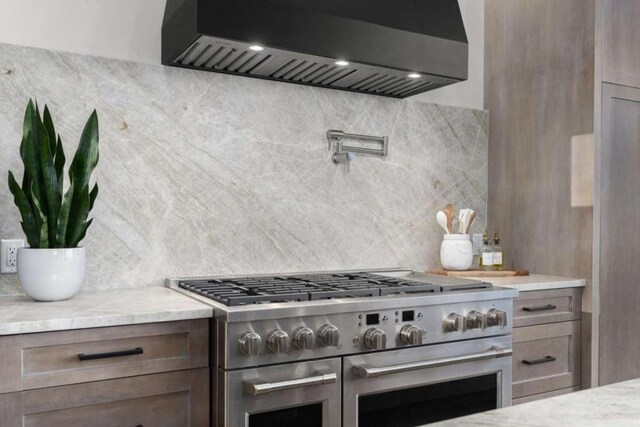 kitchen featuring tasteful backsplash, double oven range, wall chimney range hood, and light stone counters