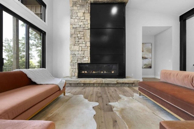 living room featuring a stone fireplace, a towering ceiling, and hardwood / wood-style flooring