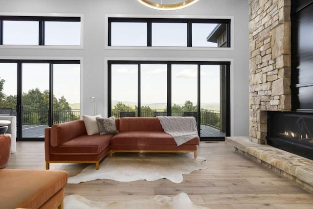 living room featuring a stone fireplace, a wealth of natural light, a high ceiling, and light wood-type flooring