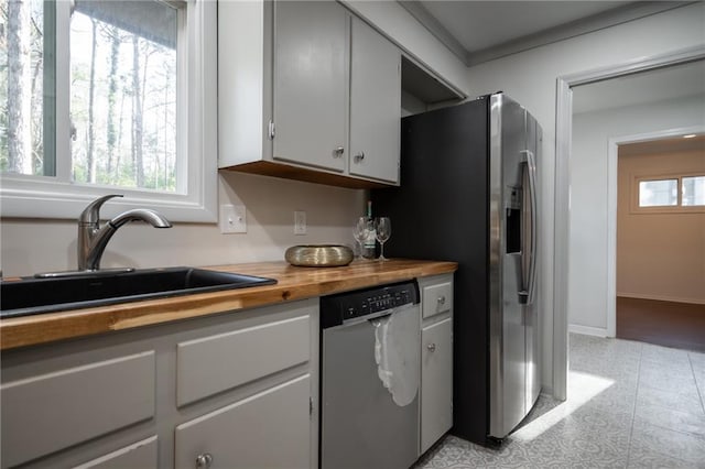 kitchen featuring stainless steel dishwasher, butcher block counters, sink, and a wealth of natural light