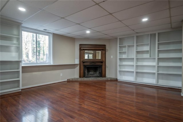 unfurnished living room with dark hardwood / wood-style floors, a paneled ceiling, and built in shelves