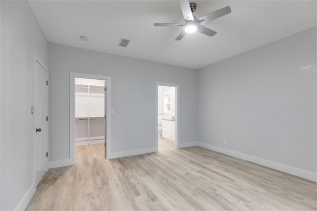 unfurnished bedroom with a closet, visible vents, light wood-style flooring, a spacious closet, and baseboards