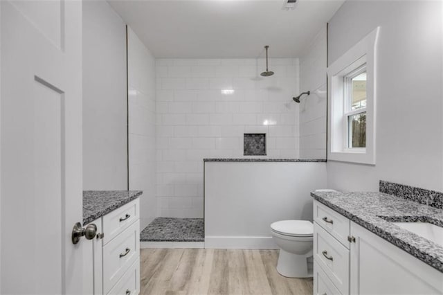 bathroom featuring toilet, a walk in shower, wood finished floors, and vanity