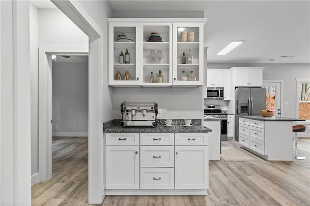 kitchen with light wood finished floors, appliances with stainless steel finishes, glass insert cabinets, and white cabinets