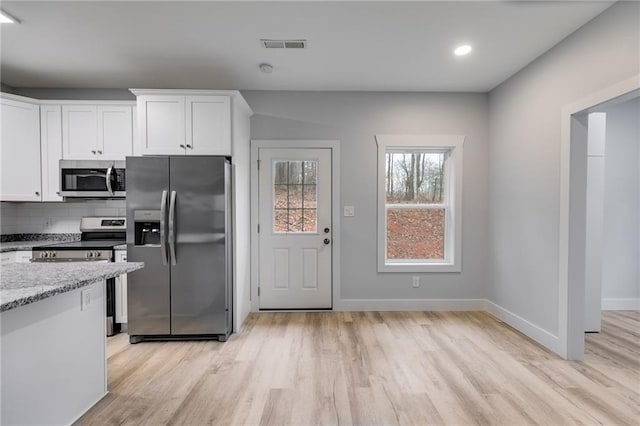 kitchen with white cabinets, light wood-type flooring, tasteful backsplash, and stainless steel appliances