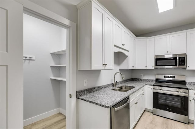 kitchen with stainless steel appliances, light wood-style flooring, a sink, light stone countertops, and baseboards